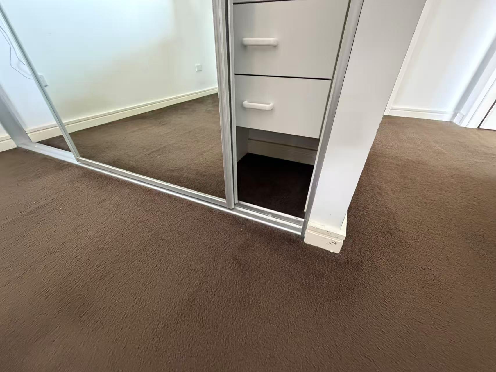Brown carpet meeting a mirrored wardrobe and drawers